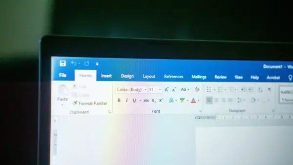 Ekran laptopa z otwartym edytorem tekstu. Widoczna jest wstążka z opcjami, w tym czcionka Calibri.