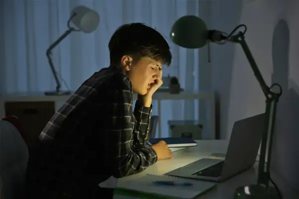 Chłopiec przy biurku, zrezygnowany, zmęczony. Czyżby padł ofiarą cyberprzemocy?