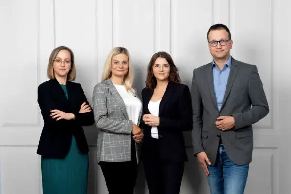Cztery osoby w strojach biznesowych stoją obok siebie na jasnym tle.