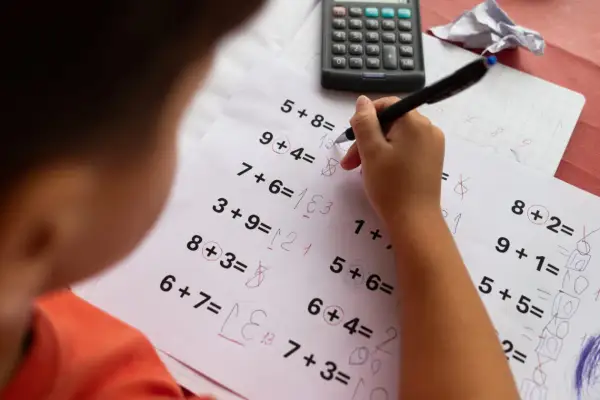 Dziecko rozwiązuje zadania matematyczne, które mogą być częścią dyskalkulia testu. Widoczny jest arkusz z działaniami i kalkulator.