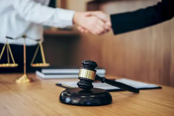 Młotek sędziowski i waga sprawiedliwości symbolizują prawo. Uścisk dłoni sugeruje porozumienie, być może w kontekście odpowiedzialności subsydiarnej.